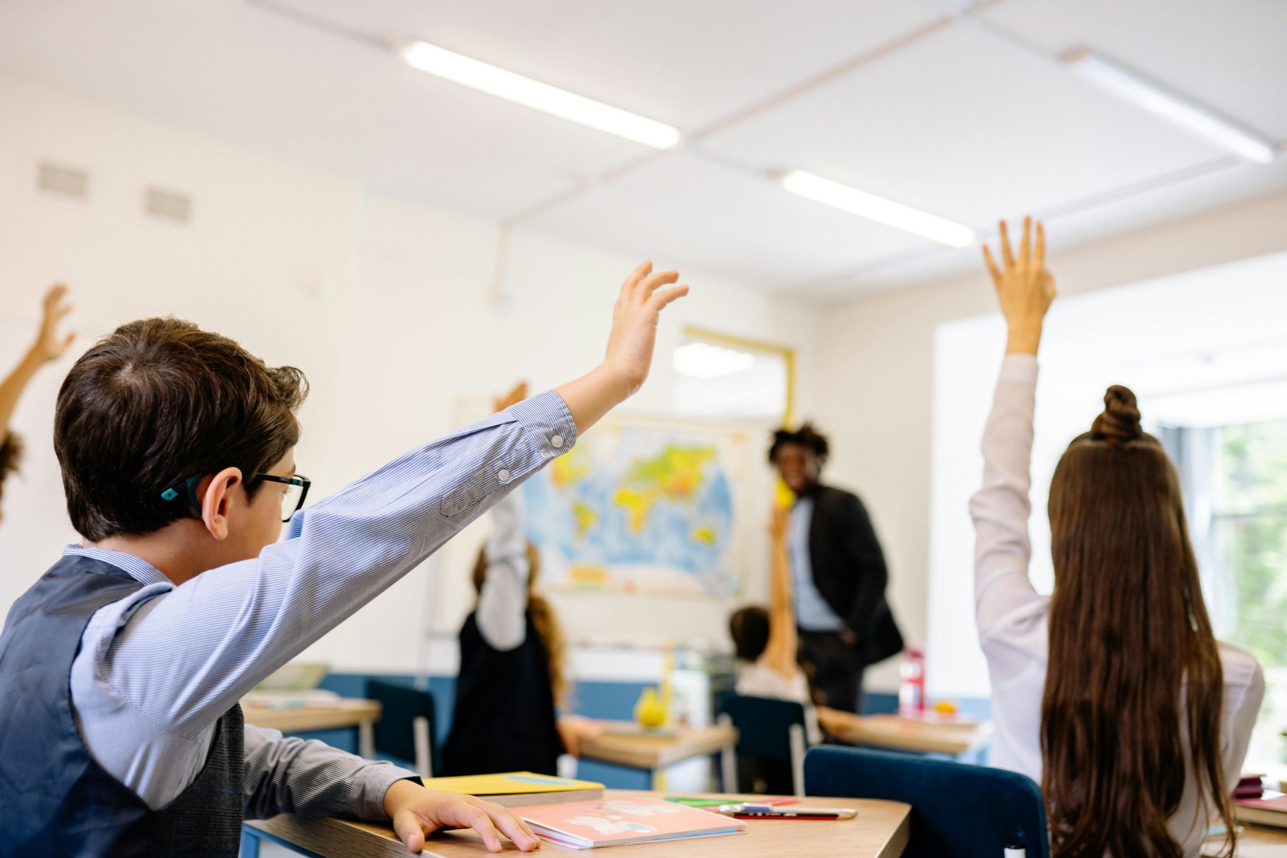 Classroom featuring children with their hand up answering teacher question